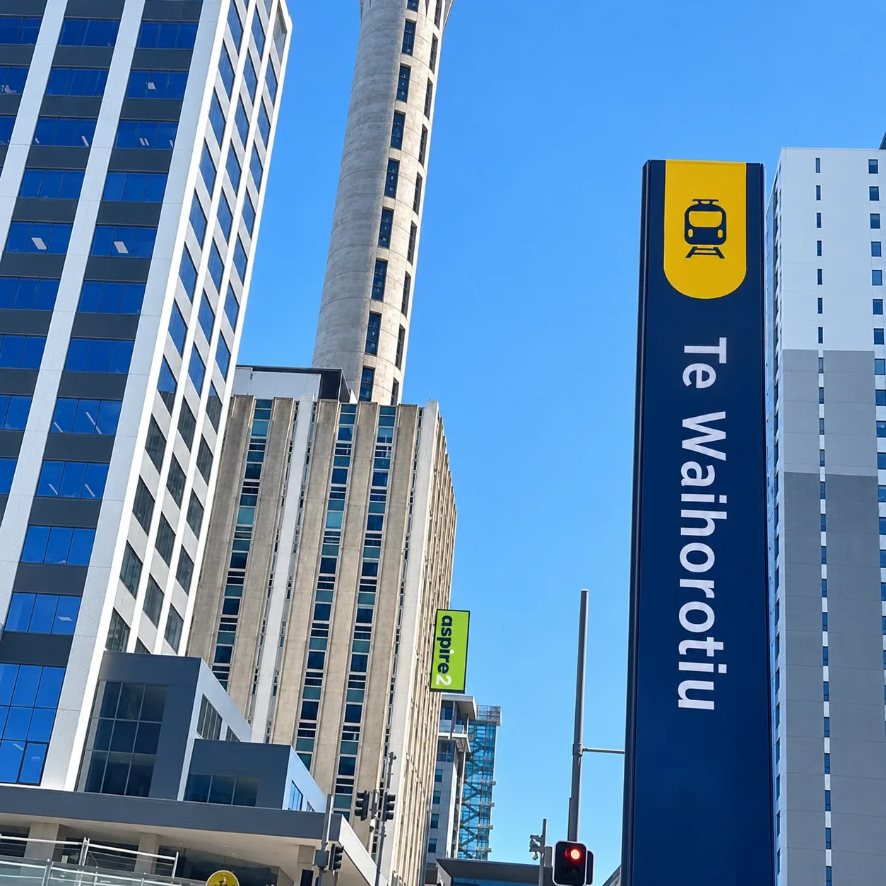 Our campus building with the Aspire2 sign, next to the Sky Tower and a Te Waihorotiu train station sign