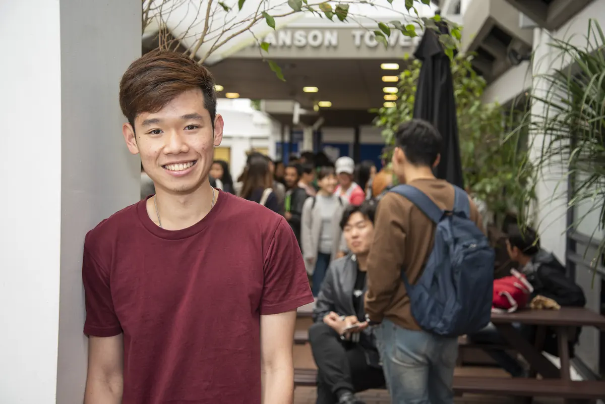 A smiling student leaning against a pillar in the campus courtyard