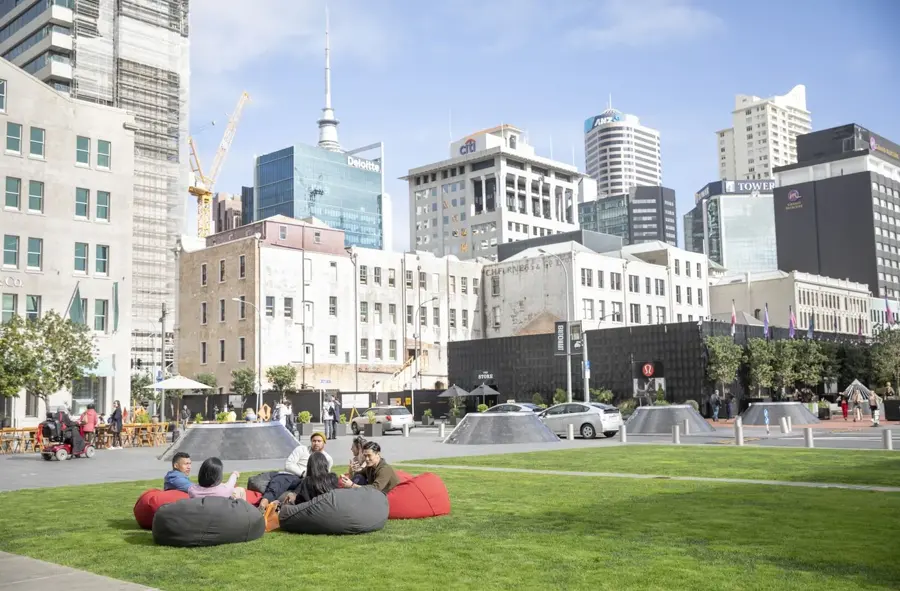 Friends relaxing on beanbags on the grass at Britomart, with the Sky Tower and city skyline behind